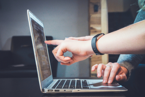 Hand pointing at a computer screen.