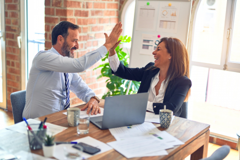 Business partners high-fiving over conference table.